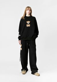 Sudadera y pantalones negros de tela suave, con un diseño de oso y detalles en contraste. Corte holgado y cómodo con cordón ajustable.