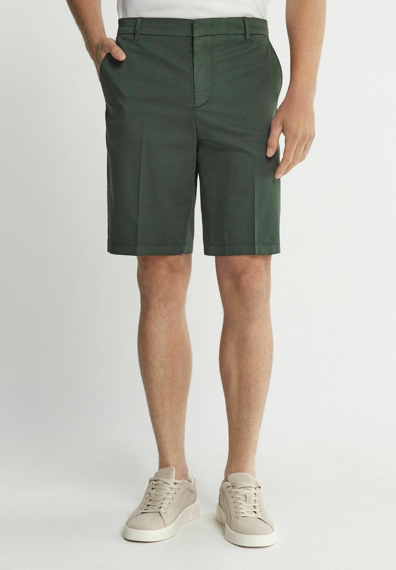 Gröna shorts gjorda av lättviktigt tyg, med platt front, sidofickor och rak skärning, kombinerade med beiga sneakers.