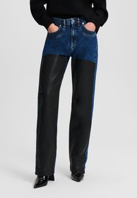 Jeans in kombinaciji z dolgimi hlačami iz črne umetne usnjene tkanine s ravnim krojem. Imajo zgornji del iz modrega jeansa in gladke črne spodnje panely.