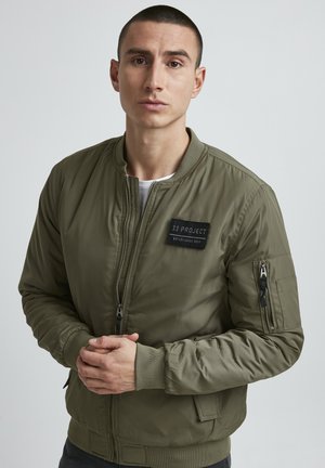 Olivgrüner Bomberjacke mit Reißverschluss vorne, gerippten Bündchen und einem Patch-Label. Verfügt über seitliche und Armtaschen mit Reißverschluss. Glatte Textur.