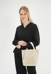 Beige ruskinds taske med et rundt håndtag og en lynlåslukning. Glat overflade med en let glans og minimalistisk design.