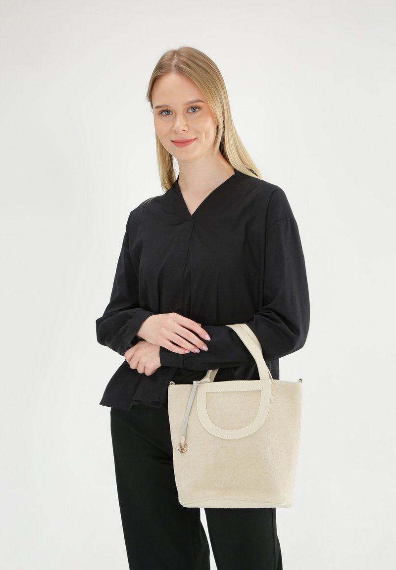 Beige ruskinds taske med et rundt håndtag og en lynlåslukning. Glat overflade med en let glans og minimalistisk design.