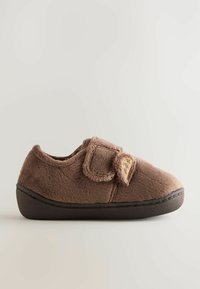 Chaussons en fourrure marron avec une sangle Velcro, de forme arrondie, semelle en caoutchouc noir, et un petit accent décoratif près de la sangle. Texture douce.