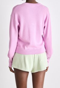 Suéter de punto rosa claro con textura acanalada y puños, combinado con pantalones cortos verde menta. Vista desde la parte trasera, mostrando el corte holgado.