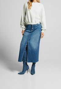 Felpa grigia chiara con polsini a costine; gonna di jeans lunga con spacco frontale e tonalità blu; abbinata a stivali blu con tacco alto.