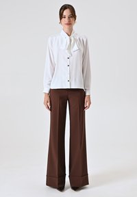 Witte blouse met een strikdetail, knoopsluiting en lange mouwen, gecombineerd met hooggetailleerde bruine wijde broek, van een gladde stof.