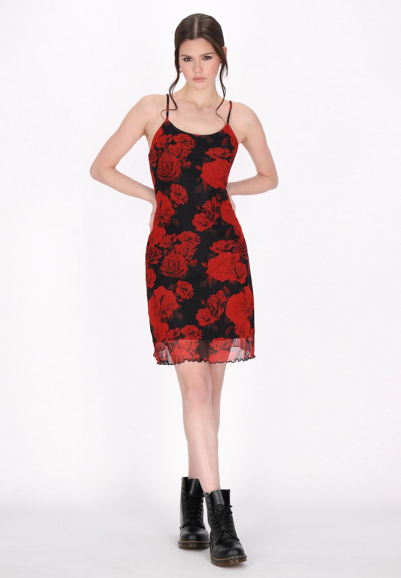 Vestido negro con estampado floral rojo, tirantes finos, silueta ajustada, dobladillo transparente y bordes con forma de concha. Combinado con botas negras de cordones.