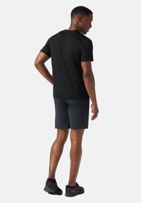 Camiseta deportiva negra de manga corta, combinada con pantalones cortos oscuros y zapatillas negras. Presenta un cuello redondo y un diseño ajustado.