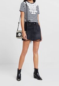 Raittikuvioinen tummansininen ja valkoinen t-paita, jossa on pitsimuotoilu, yhdistettynä korkeavyötäröiseen mustaan farkkuhameeseen, jossa on frayed-reunat. Mustat nilkkasaappaat.