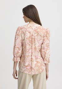 Blusa a fantasia floreale in tessuto leggero con tonalità di rosa e beige. Presenta maniche a sbuffo a tre quarti e scollatura arrotondata sul retro.
