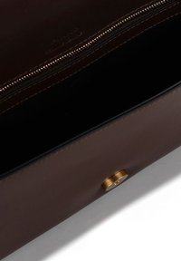 Borsa in pelle marrone con chiusura a zip e dettaglio con bottone metallico. L'interno è scuro, mostrando una texture liscia e un design minimalista.
