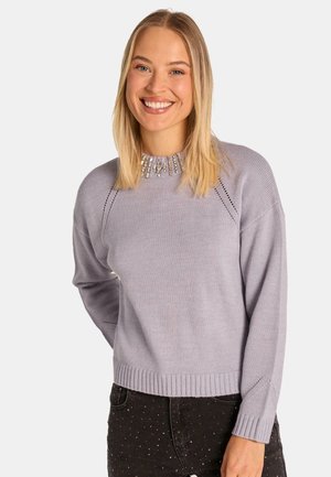 Suéter de lavanda claro con un patrón texturizado cerca del cuello, con puños y dobladillo acanalados. Lleva puesto encima de pantalones negros con puntos blancos.