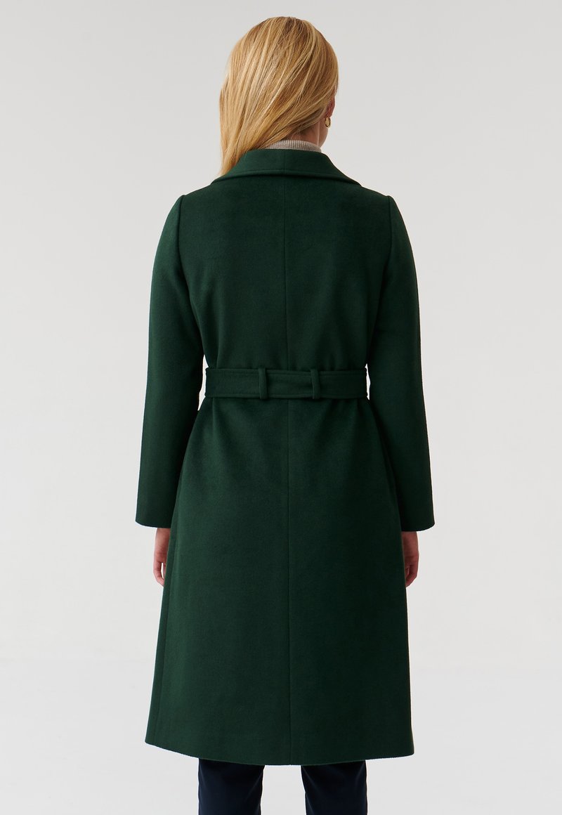 Cappotto lungo in misto lana di un verde scuro, con vita fasciante e colletto a rever. Tessuto liscio, maniche lunghe e orlo dritto.