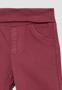 Bordeauxrode broek met een zachte textuur, voorzien van een brede tailleband en een voorkeeltas. De stof heeft een lichte glans en stevige stiksels.