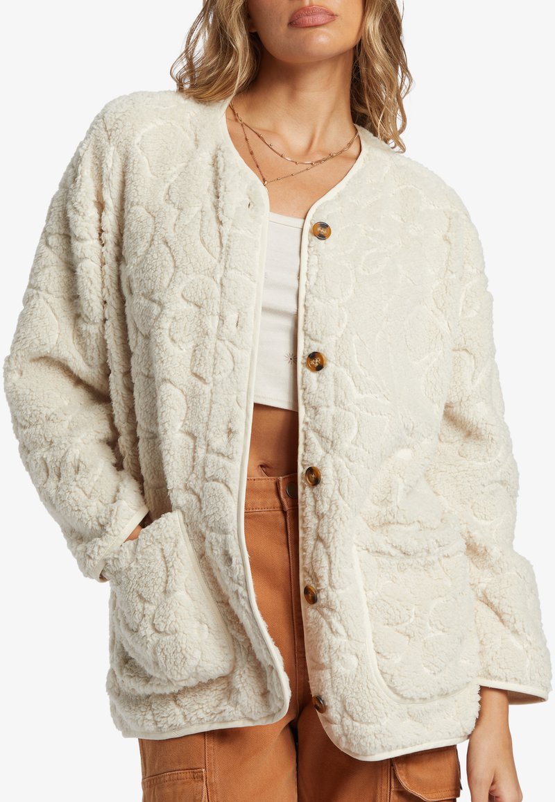 Cardigan di colore crema con texture, motivi floreali, bottoni a scatto e due tasche frontali. Realizzato in materiale morbido e soffice.