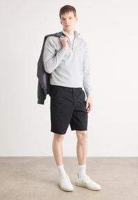 Šedý pletený svetr na zip přes bílou tričko, spárován s černými šortkami. Bílé tenisky a kotníkové ponožky dokončují outfit.