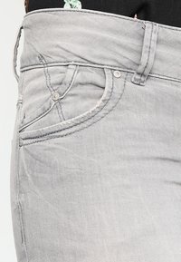 Jeans en denim gris avec une silhouette ajustée, dotés d'une fermeture à boutons, de poches cousues et d'une texture douce.
