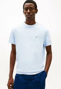 Camiseta de algodón azul claro de cuello redondo y mangas cortas. Presenta un pequeño logotipo en el pecho. La tela tiene una textura suave.