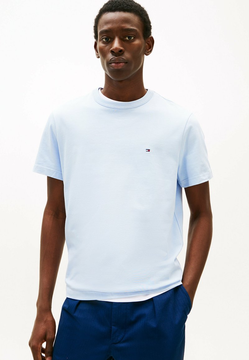 Camiseta de algodón azul claro de cuello redondo y mangas cortas. Presenta un pequeño logotipo en el pecho. La tela tiene una textura suave.
