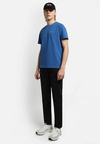T-shirt di cotone blu abbinata a pantaloni neri. Un cappellino nero con design della bandiera norvegese. Le calzature presentano accenti grigi e bianchi.
