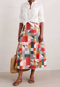 Chemise en lin nouée à la taille, assortie à une longue jupe patchwork colorée avec des motifs géométriques rouges, verts, gris et blancs.