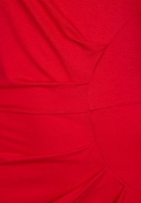 Tessuto di colore rosso con sezioni arricciate e superfici lisce, caratterizzato da un dettaglio circolare prominente e sottili variazioni tonali in tutto il materiale.