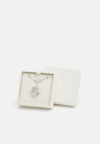 Colar de prata com um pingente circular ornamentado numa caixa de joias, apresentando uma pedra clara e detalhes geométricos intrincados.