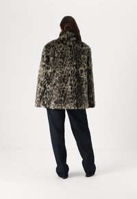 Plašč iz umetnega krzna v leopardskem vzorcu z visokim ovratnikom, sproščenim krojem in dolgimi rokavi, v kombinaciji s temnimi jeans hlačami.