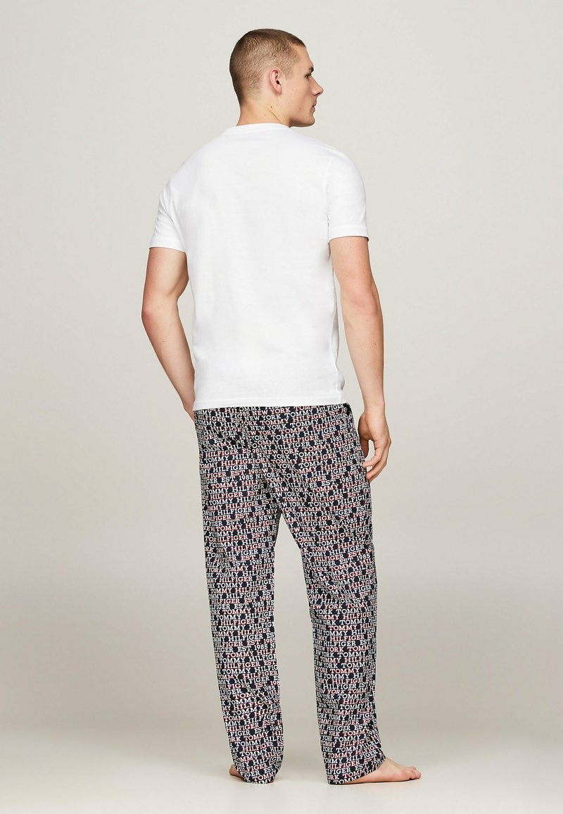 Witte korte mouwen T-shirt voor mannen gecombineerd met zwarte pyjamabroek met patroon met rode en witte tekst. Stof lijkt glad; ontspannen pasvorm.