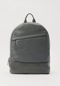 Mochila de cuero gris con parte superior redondeada, bolsillo frontal con cremallera y detalles sutiles de costura. Cuenta con asa superior y correas ajustables.