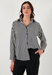 Black and white striped button-up shirt with a collar, long sleeves, and a relaxed fit, featuring vertical stripes and a slightly curved hem.