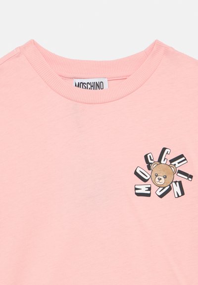 Ροζ βαμβακερό μπλουζάκι με στρογγυλή λαιμόκοψη και γραφική απεικόνιση αρκούδου με το κείμενο "MOSCHINO" σε παιχνιδιάρικη γραμματοσειρά στο ύψος του στήθους.