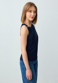 Top senza maniche navy con scollo a barca, caratterizzato da un accento dorato sulla spalla. Tessuto liscio con un design aderente.