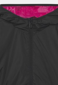 Chaqueta ligera negra con un interior rosa. Presenta un cierre delantero, capucha y textura suave. Diseño minimalista sin patrones visibles.