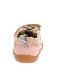 Zapato de cuero y ante rosa con parte posterior redondeada, acentos grises y una correa de velcro. Suela de goma con textura para mayor agarre.