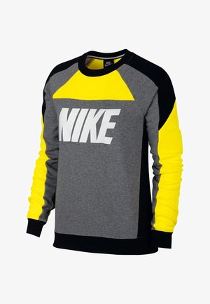 Sudadera Nike con un diseño en bloques de color que incluye paneles en gris, negro y amarillo brillante. Gran logo blanco en la parte delantera. Textura suave.