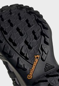 Gros plan de la semelle noire d’une chaussure Adidas avec un motif de bande de roulement robuste et un logo orange Continental au niveau du talon.