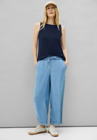 Marineblaues, geripptes, ärmelloses Top kombiniert mit hellblauen, weit geschnittenen Jeans, die über einen elastischen Bund und seitliche Taschen verfügen. Getragen mit weißen Turnschuhen.