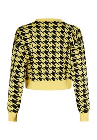 Žltý krátky sveter s čiernym houndstooth vzorom. Má dlhé rukávy a rebrovaný lem. Mäkko pletený povrch.