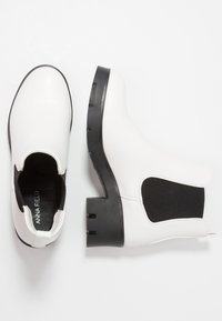 Bílé kožené kotníkové boty s elastickými bočními panely, černými gumovými podrážkami a blokovým podpatkem. Má minimalistické prošívání a elegantní design.