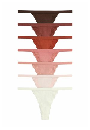 Kvinde med skulderlangt hår løfter sin hvide camisole for at afsløre mauve blondeundertøj mod en ensfarvet lys baggrund.
