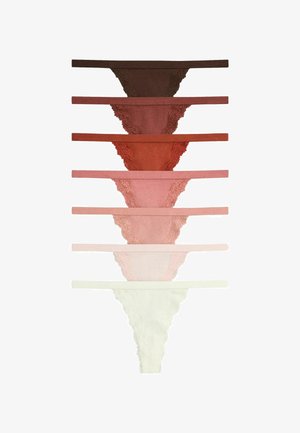 Kvinde med skulderlangt hår løfter sin hvide camisole for at afsløre mauve blondeundertøj mod en ensfarvet lys baggrund.