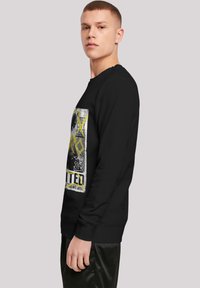 Sudadera negra con estampado gráfico que presenta texto e imágenes en amarillo y blanco, cuello redondo y puños acanalados. Textura de tela suave.