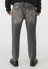 Černé džínové kalhoty s vybledlým, vyšisovaným vzhledem, viditelným prošíváním a zadními kapsami, doplněné uvolněným střihem s rovnými nohavicemi.