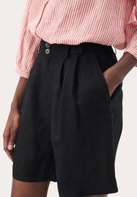 Zwarte linnen shorts met een hoge taille, twee knopen, plooien aan de voorkant en zijzakken. Gestyled met een roze en witte gestreepte top.