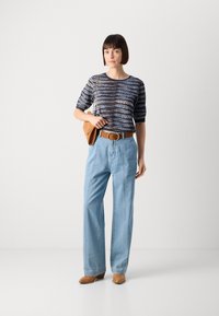 Marine mønstrete strikket topp med korte ermer, lys blå vide denimjeans, brun lærbelte og beige hæl mules, som holder en brun veske.