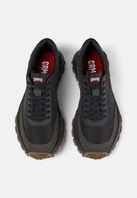Pair of black Camper sneakers with brown rubber soles and red insoles, viewed from above, showing laces and brand logo on tongues.