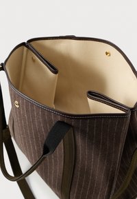 Rudas dryžuotas audinys tote krepšys su šviesiu vidumi, dviem skyreliais ir juodais bei alyvuogių žaliais dirželiais. Matomi auksiniai akcentai.