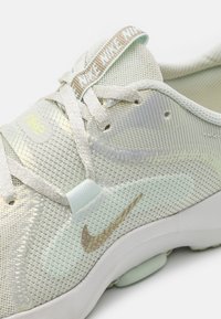 Light green Nike sneaker with mesh upper, reflective accents, cream laces, and silver swoosh. Features padded collar and textured sole.