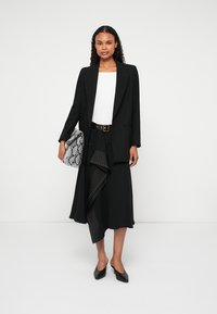 Melna žakete virs baltas topa, apvienota ar melnu svārku ar asimetrisku dizainu un studētiem akcentiem. Aksesuārs: čūskas drukas rokassoma.